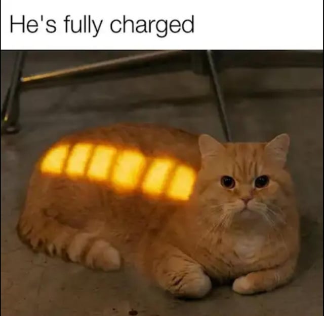 This meme features an orange tabby cat lying on a concrete floor under a chair. Sunlight filtered through blinds creates six bright rectangular yellow bars across the cat's back, which exactly resembles a fully charged battery icon from a digital device. The text at the top reads 'He's fully charged', making a cute joke that the cat has fully recharged its energy by soaking up sunlight, just like an electronic device.