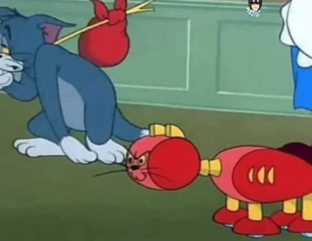 This is a still screenshot from the classic animated series *Tom and Jerry*. The blue cat Tom stands looking dejected and defeated, carrying a traditional bindle (a stick with a tied red cloth sack slung over his shoulder, culturally associated with being fired, evicted, or leaving a place permanently) over his shoulder. In front of him sits a red robotic cat device designed to catch mice, which has replaced Tom in his role as the house's pest control. The meme jokes that Tom is the first entity to lose his job to artificial intelligence/automation, playing on modern widespread anxieties about AI displacing human workers across industries.