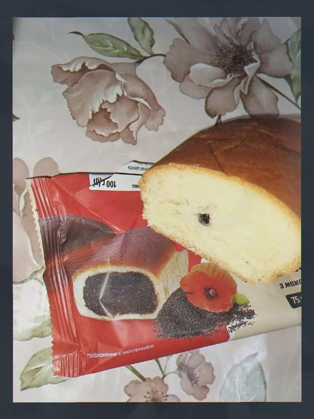 The image displays a comparison between the advertised product on a poppy seed bun package and the actual bun received after opening. The packaging illustration shows a bun stuffed with a large, generous portion of poppy seed filling, while the real sliced bun next to it only contains one tiny single poppy seed as filling. The stark contrast between the promised product and the real item creates a humorous joke about misleading food packaging and unmet consumer expectations. Small fine print on the package in Russian notes the packaging image is just an illustration, further emphasizing the joke about misleading advertising.