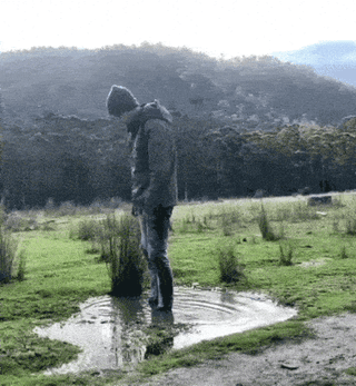 An outdoor scene set in a grassy field with forested hills in the background shows a person in casual outdoor wear standing in a shallow muddy puddle. They leap upward to attempt a backflip, but miscalculate their movement, landing directly face-first in the muddy puddle. After the impact, the person lies completely flat and motionless in the mud, appearing to give up entirely, matching the meme's title of finding peace after the failed stunt. The humor derives from the anticlimactic, still end to the ambitious flip attempt, playing on the joke that being too tired to move after an embarrassing failure feels like peace.