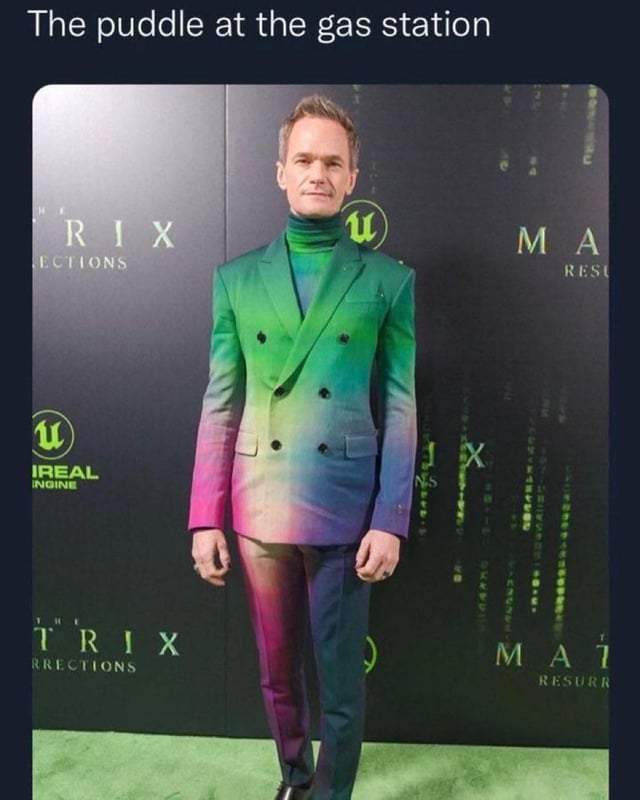 A meme featuring a red carpet photograph from 'The Matrix Resurrections' premiere, showcasing Neil Patrick Harris wearing a vibrant gradient suit transitioning from green to pink, purple, and blue. The top text reads 'The puddle at the gas station,' creating a humorous analogy between the colorful suit and the iridescent rainbow sheen of oil puddles commonly observed at gas stations.