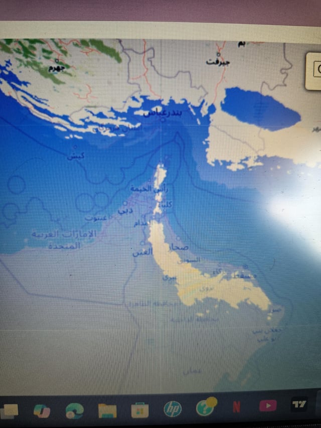This image is a photograph of a desktop computer screen showing an interactive map simulation of 450 meters of global sea level rise applied to the Persian Gulf and Arabian Peninsula region. Most of the low-lying coastal land around the Strait of Hormuz is submerged by water, which results in the strait becoming completely unobstructed by surrounding land. The meme jokes that this extreme, catastrophic sea level rise is an absurd 'solution' to geopolitical tensions and blockades of the Strait of Hormuz. All place labels on the map are written in Arabic.