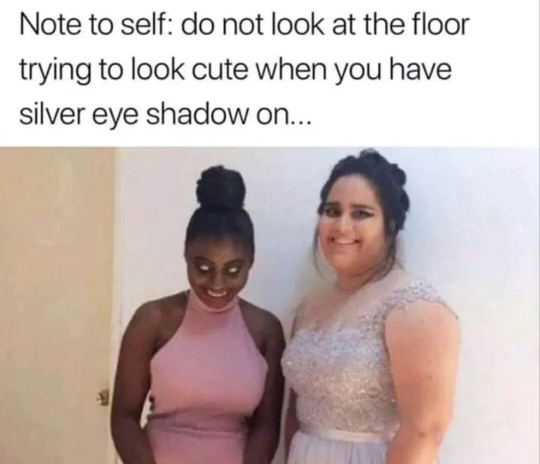 This meme features a top text warning paired with a photo of two women posing in formal dresses. The text is a personal note: do not look down toward the floor when trying to take a cute photo if you are wearing silver eyeshadow, particularly if you have dark skin. In the photo, the Black woman on the left appears to have unnaturally glowing solid white eyes: this effect is caused by silver eyeshadow reflecting bright ambient light from the light-colored floor, creating an unintended spooky supernatural-looking effect, while the woman standing next to her smiles normally. The joke comes from the unexpected funny and creepy result of an accidental makeup and lighting mishap.