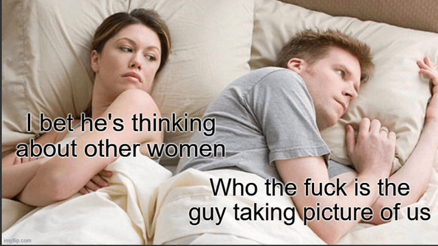 This meme uses the popular 'couple lying in bed' stock photo template, showing a woman and man lying side by side under covers, both looking thoughtful and facing opposite directions. The caption over the woman follows the standard template trope, reading 'I bet he's thinking about other women', referencing the common comedic premise that women assume their distant male partners are thinking of romantic rivals. The caption over the man completely subverts this trope, reading 'Who the fuck is the guy taking picture of us', pointing out the logical absurdity of an unseen third person being present to take a photo of the couple in their private bedroom, breaking the fourth wall of the meme format for a comedic twist.