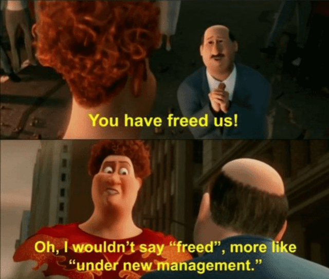 A two-panel meme using animated screenshots, likely from the 2010 film 'Megamind'. The top panel shows a bald man in a suit clasping his hands, facing a character with curly red hair (viewed from behind), with yellow text: 'You have freed us!'. The bottom panel reveals the red-haired character (now facing forward, wearing a red shirt) responding with yellow text: 'Oh, I wouldn't say "freed", more like "under new management."'. The urban street setting with buildings suggests a city environment. The meme humorously implies a situation where a perceived liberation is actually just a transfer of authority.