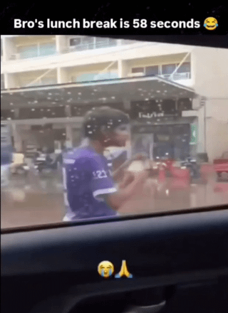 This is a candid meme photograph taken from inside a vehicle, looking out through a slightly spotted car window. It shows a food delivery worker wearing a purple uniform walking along a street while quickly eating food during their break. The meme is overlaid with text at the top reading "Bro's lunch break is 58 seconds 😂", plus crying laughing and prayer hand emojis at the bottom. The original title "Cancer speedrun" is a dark joke referencing that the extremely short, rushed break time and harsh working conditions of gig economy delivery workers will lead to serious health issues at a rapid pace, as if they are "speedrunning" developing chronic illnesses like cancer from overwork and poor self-care habits forced by their job.