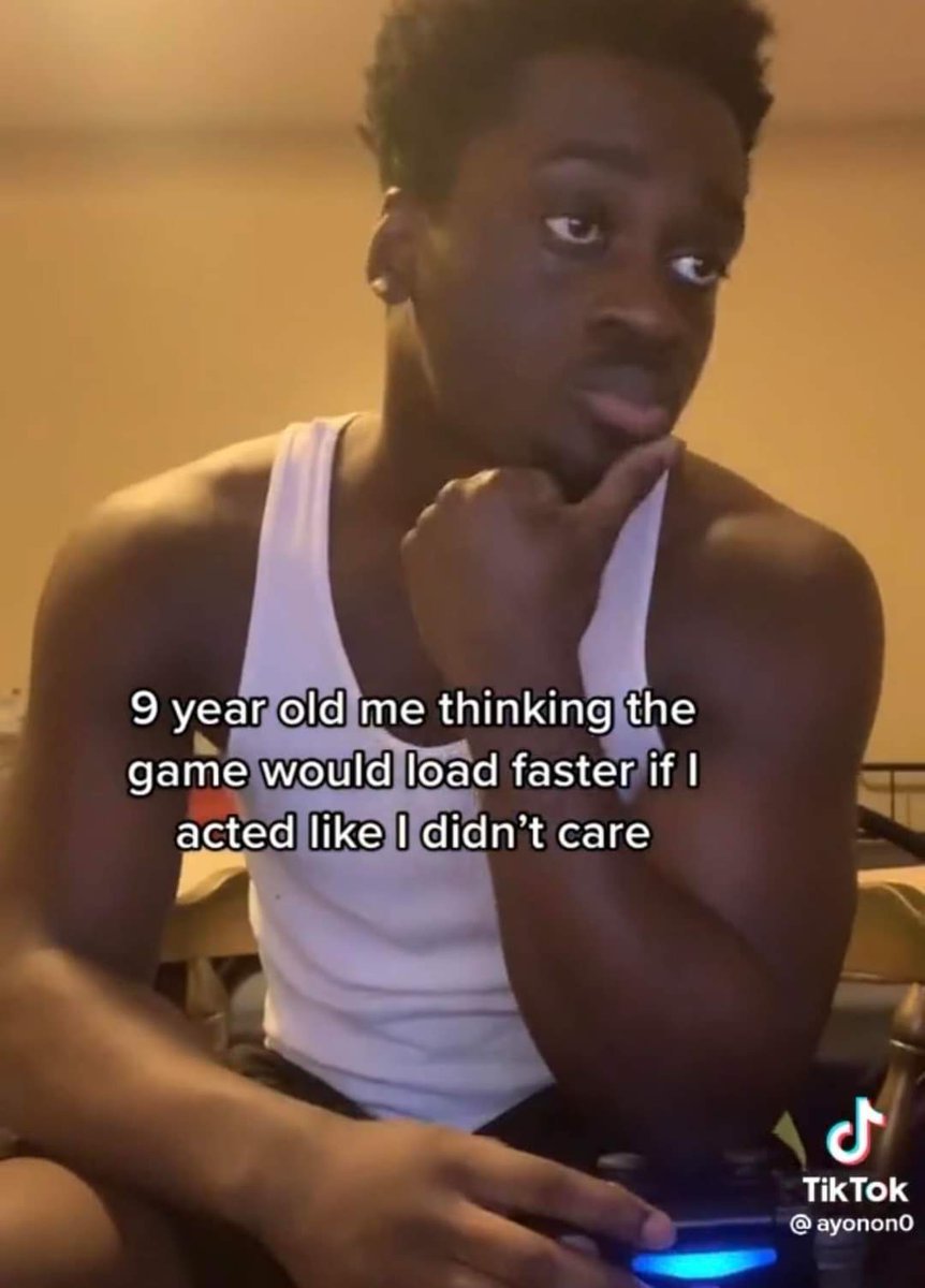 The meme features a young Black man wearing a white tank top, holding a lit PlayStation controller while resting his chin on his hand and looking off to the side with an exaggerated, deliberately uninterested expression. Overlaid white text on the image reads "9 year old me thinking the game would load faster if I acted like I didn't care", referencing the widely relatable childhood superstition that ignoring a loading video game would make it finish loading more quickly. The joke resonates with people who grew up playing video games with long load times, highlighting the silly, irrational behaviors many children adopted out of impatience.