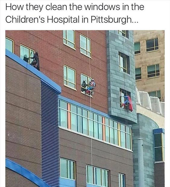 A photograph of window cleaners rappelling down the exterior of Pittsburgh Children's Hospital. The multi-story building features a mix of brick and modern architectural elements with large, colorful windows, creating a child-friendly environment. Several cleaners are visible on ropes; one appears to interact—likely waving or gesturing—towards individuals inside the windows, implying engagement with children. The text at the top frames the scene as a heartwarming example of everyday kindness in a healthcare setting, highlighting positive human connection between workers and young patients.