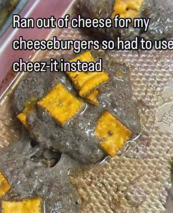 The image displays a foil-lined baking tray holding several severely overcooked, charcoal-black hamburger patties. Multiple square yellow Cheez-It cheese crackers are placed on top of the burnt patties, used as a replacement for traditional cheese slices. Overlaid white text with a black outline reads 'Ran out of cheese for my cheeseburgers so had to use cheez-it instead', highlighting the absurd, poorly executed cooking hack that resulted in completely ruined patties.