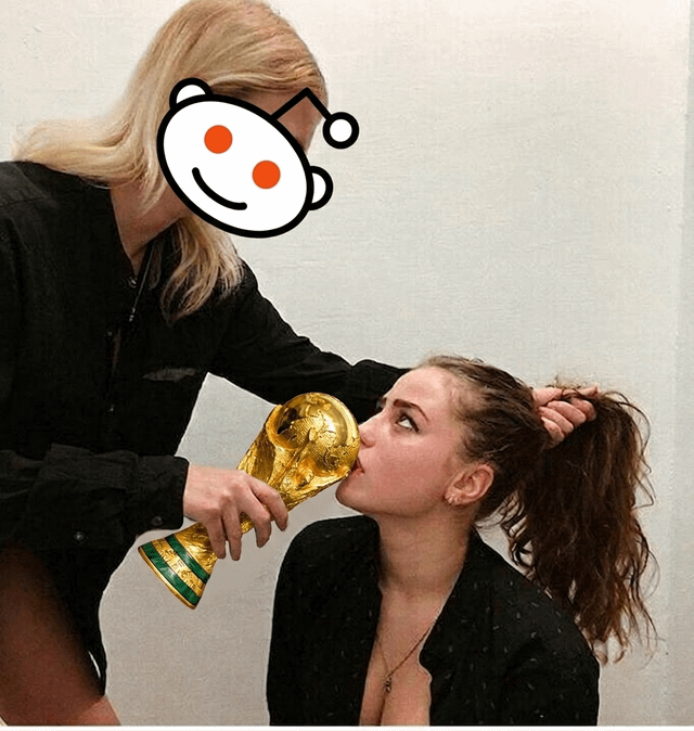 The meme shows a standing blonde woman whose face is covered by the Reddit Snoo mascot logo. She is holding the golden FIFA World Cup trophy up to the mouth of a seated brunette woman, while pulling the seated woman's hair back. The seated woman has her eyes rolled upward in a reluctant, annoyed expression as she kisses the opening of the trophy. The joke is a crude, suggestive double entendre comparing Reddit's overwhelming, over-the-top excitement around World Cup football victories to a forced lewd oral sex act.