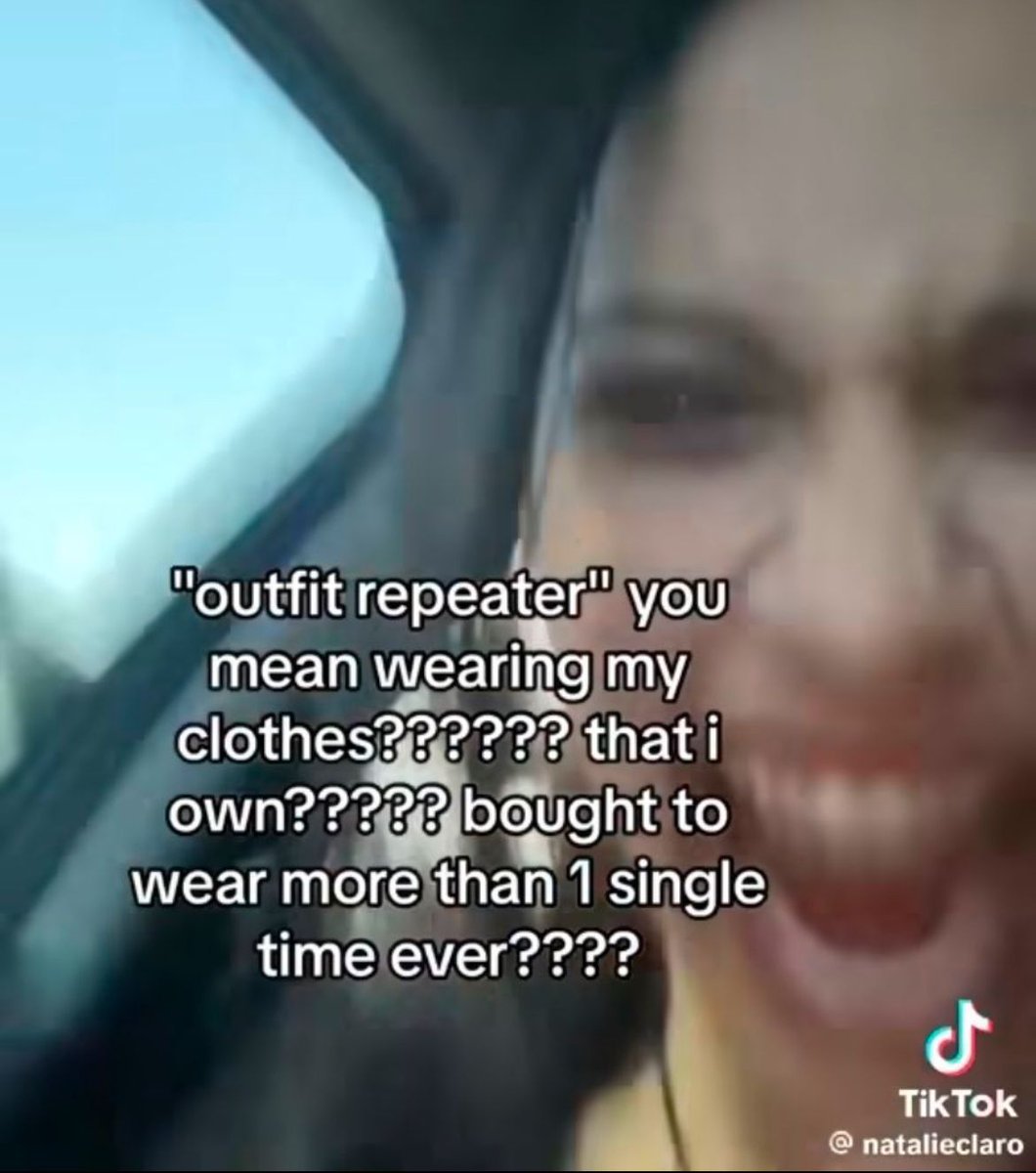 The image is a blurry close-up shot of a young woman inside a car, appearing to laugh while ranting directly at the camera. Overlaid white text expresses sarcastic disbelief at the term 'outfit repeater', pointing out that wearing clothing you purchased multiple times is the intended purpose of owning clothes, pushing back against unrealistic fashion and consumerism pressure that implies people need to wear new outfits for every occasion.
