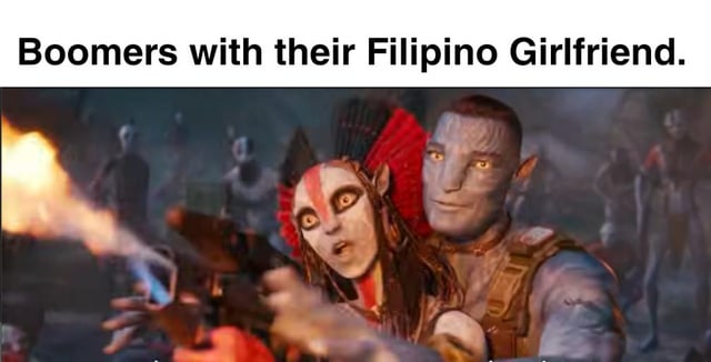 A meme image featuring two Na'vi characters from the movie 'Avatar.' The top text reads 'Boomers with their Filipino Girlfriend.' The foreground shows a female Na'vi with red and white face paint, wide eyes, and an expression of shock or surprise, holding a gun that emits flames. Behind her, a male Na'vi with a calm, smiling expression has his arm around her shoulders. The background includes other Na'vi figures in a dimly lit, forest-like environment. The meme likely uses the contrast between the shocked female and calm male to humorously reference stereotypes about boomers and their relationships.