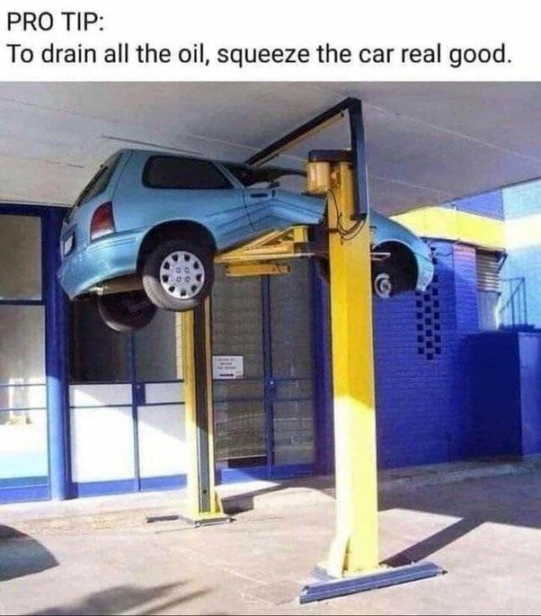 The meme features a real photograph of a light blue compact car that has been crushed between the ceiling of an auto repair shop and a yellow 2-post car lift, which was raised too high and caused the car to be squashed. Overlaid on the top of the image is sarcastic text that jokes the damaging accident is an intentional hack to fully remove all oil from the vehicle during maintenance.